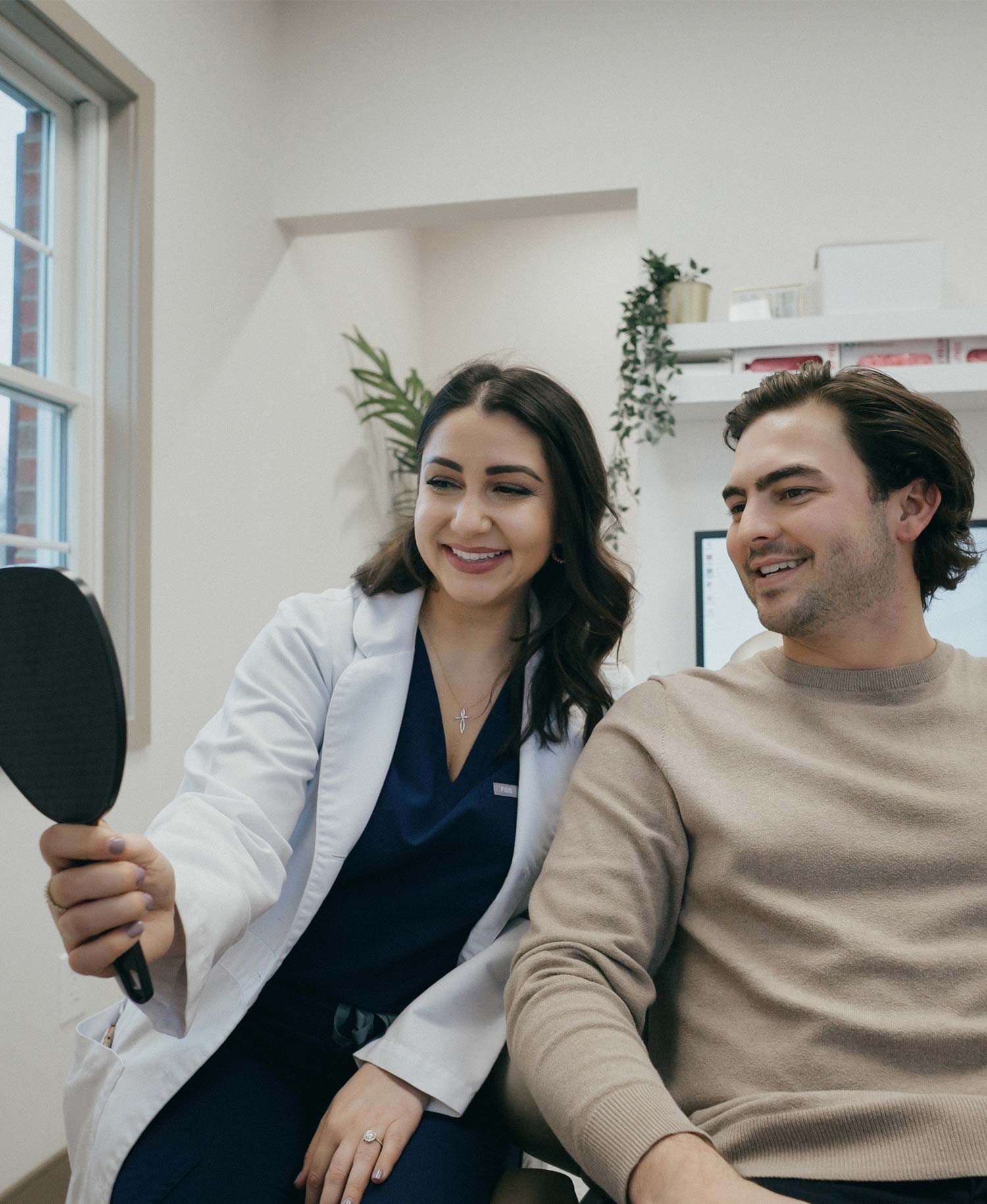 Female dentist showing a smiling male patient his reflection in a handheld mirror
